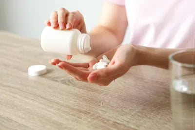 Mulher despejando cápsulas brancas de magnésio na palma da mão. 